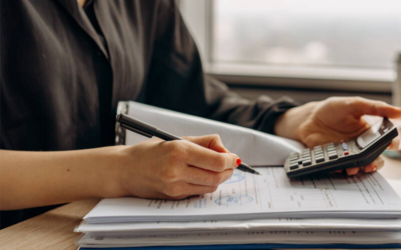 Picture of women using calculator and consulting folder of invoices