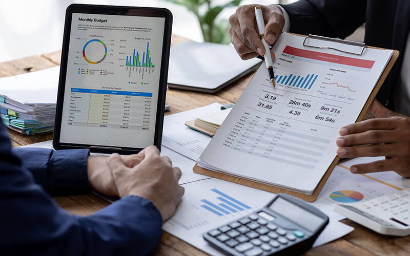 Business men looking at charts and information on paper and on the screen of a tablet computer