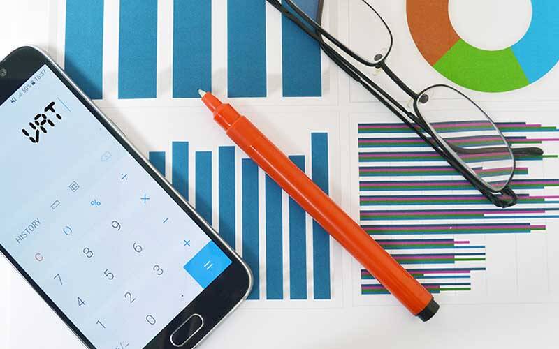 Picture of charts and information with a mobile phone with the calculator app open, a red berol pen, and a pair of spectacles