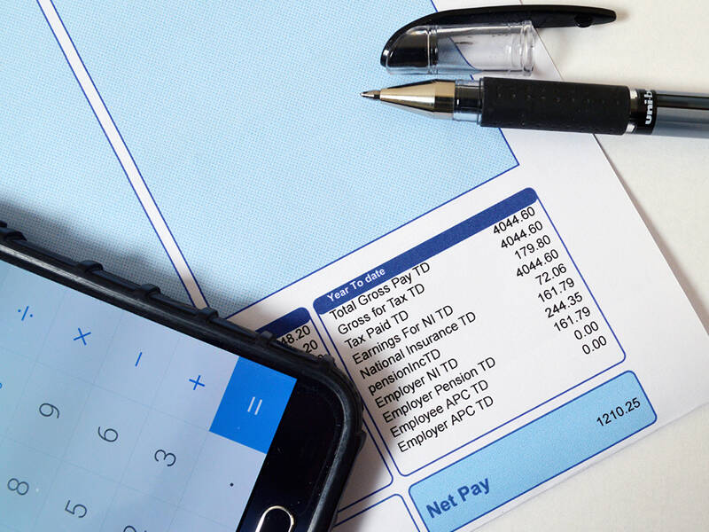 Picture of payslip, pen and mobile phone with the calculator app open