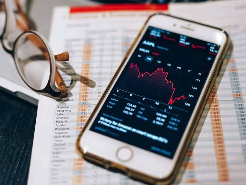 Picture of investment data paper on print outs under a mobile phone displaying investment data on the screen