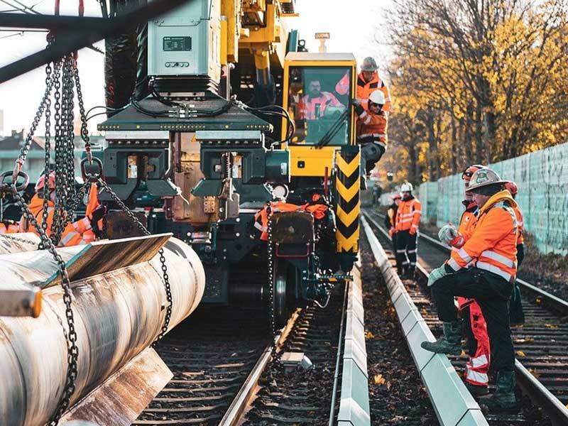 Railway workers standing on a railway lines near a crane and metal pipes