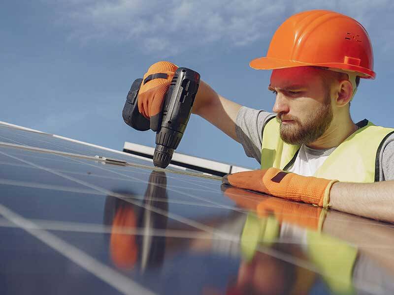 Construction worker wearing a hard hat and securing solar panels to roof top