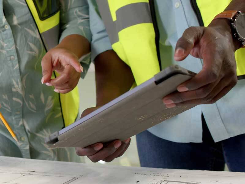 Construction workers wearing high-visiability vests and looking at a tablet computer
