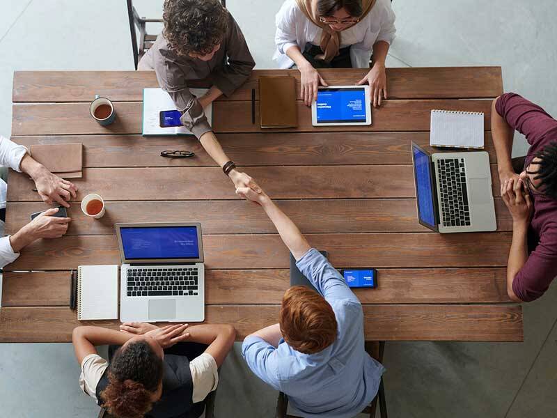 Business men and women sitting around a wooden table with latops and mobile phones