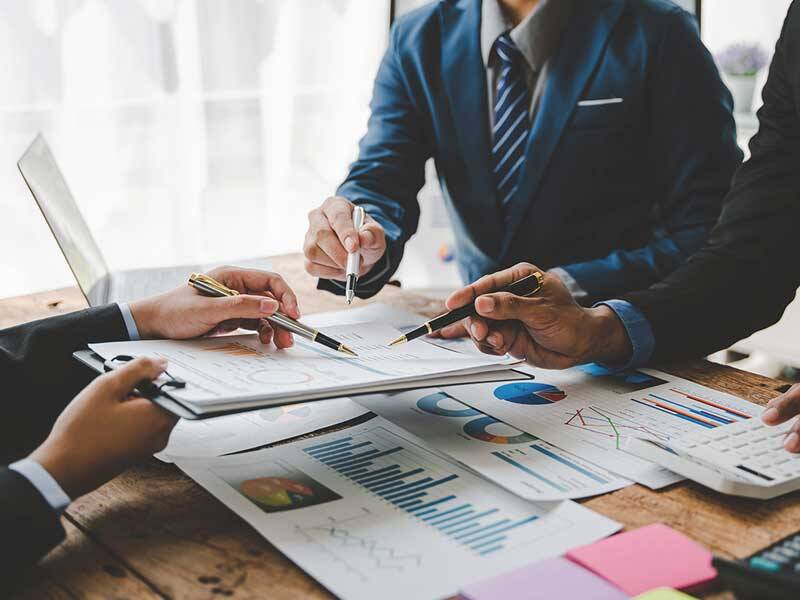 Business men holding a business meeting while looking at charts and information on a clip board, on their table and using a calculator