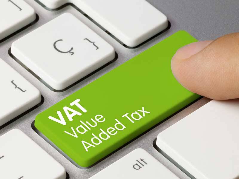 Person pointing at a green computer keyboard key with VAT Value Added Tax written